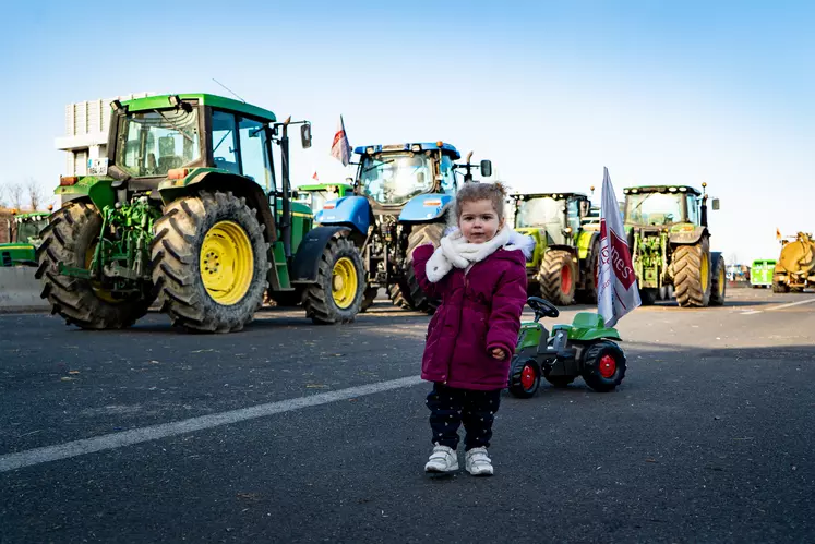 Une petite fille avec son tracteur à pédale sur l'A71 de Clermont-Ferrand, devant une file de tracteurs stationnés..