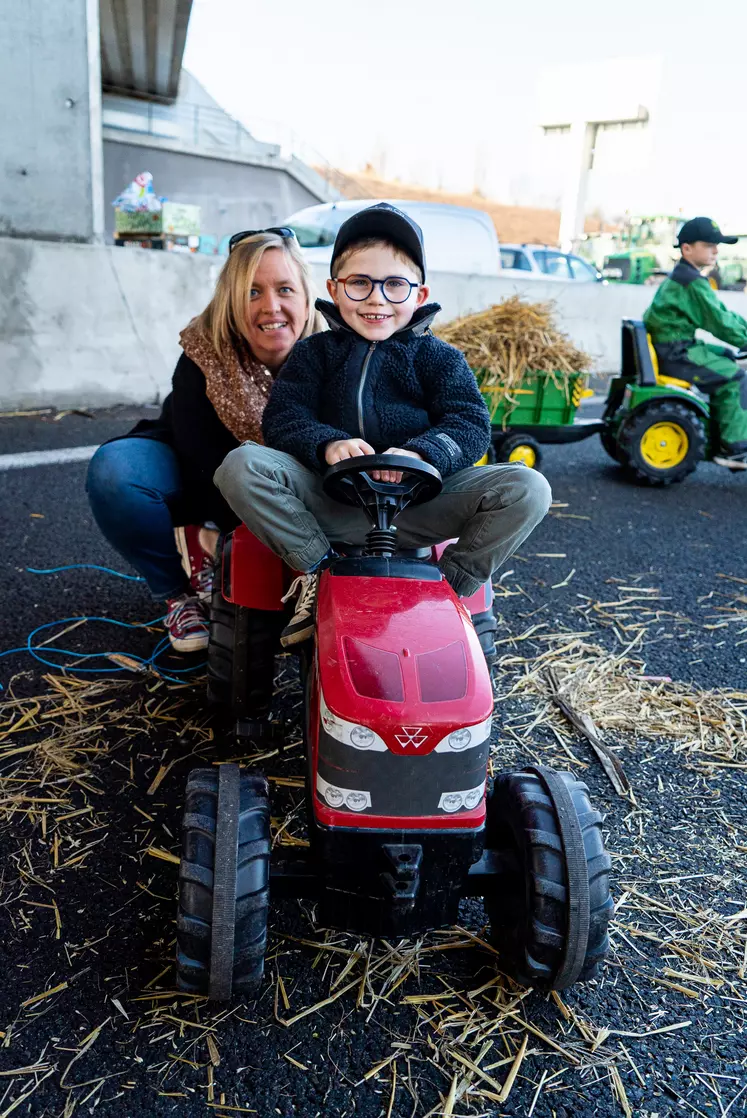Une maman avec son petit garçon sur un tracteur à pédales.