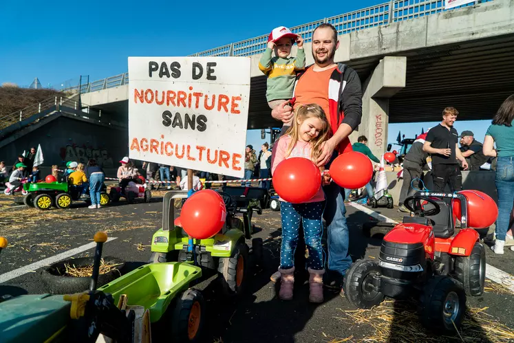 Un papa avec son petit garçon et sa petite fille devant une pancarte sur laquelle on peut lire "pas de nourriture sans agriculture".