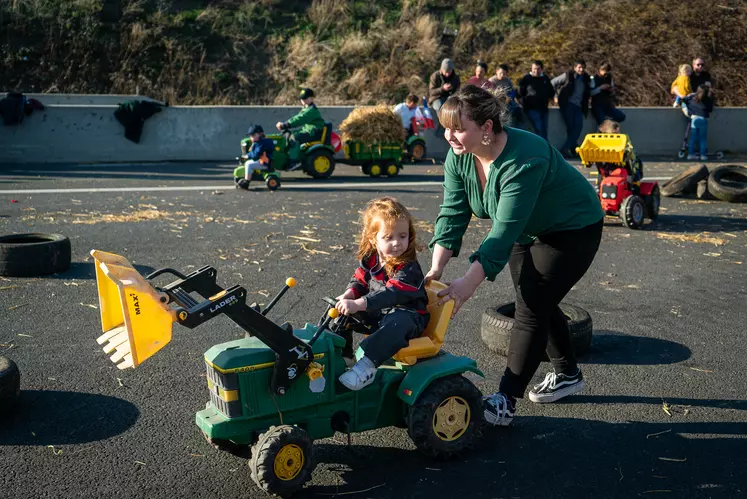 Une mère pousse sa fille, assise sur un tracteur à pédales.