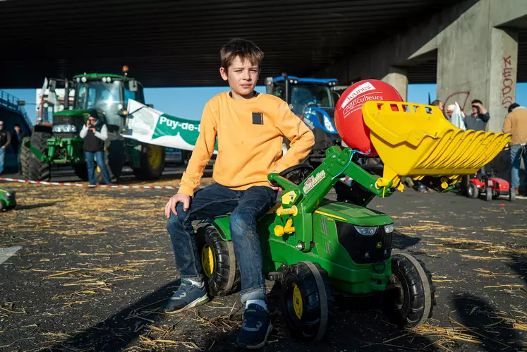 Petit garçon assis sur un tracteur à pédale.