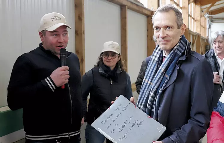 Philippe Castanet, le préfet de Lozère, tient la pochette de la pétition et la montre au photographe. À ces côtés, un adhérent du collectif contre les prairies sensibles parle dans un micro avec une casquette beige au nom du collectif sur la tête.