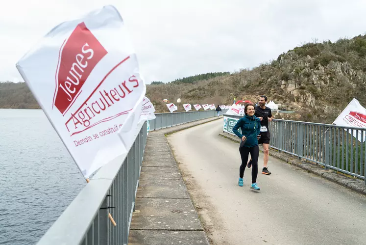 Deux coureurs sur le pont d'un barrage, un drapeau des jeunes agriculteurs au premier plan.