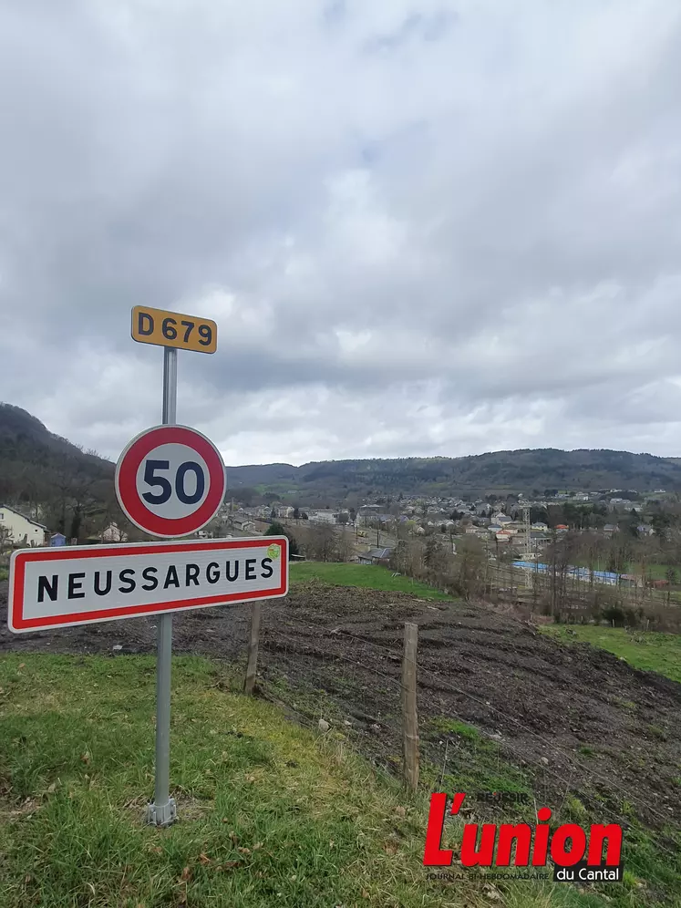 un panneau avec écrit 50 et Neussargues, en arrière plan le village