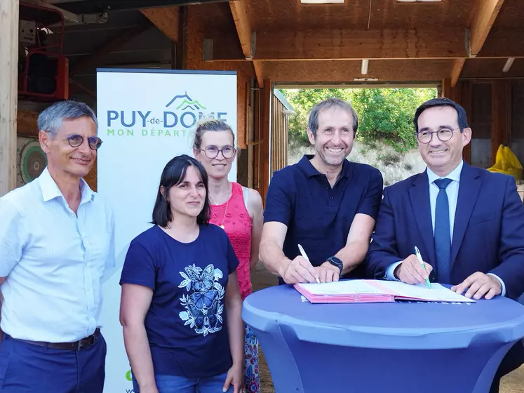 trois hommes et deux femmes souriants signent un contrat devant un panneaux du puy-de-dôme