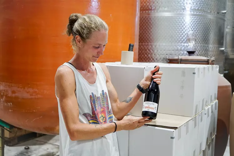 une femme devant des cuves tient un bouteille de vin