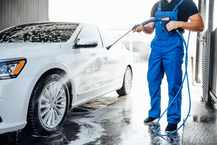 Un homme en salopette nettoie une voiture avec un jet d'eau 