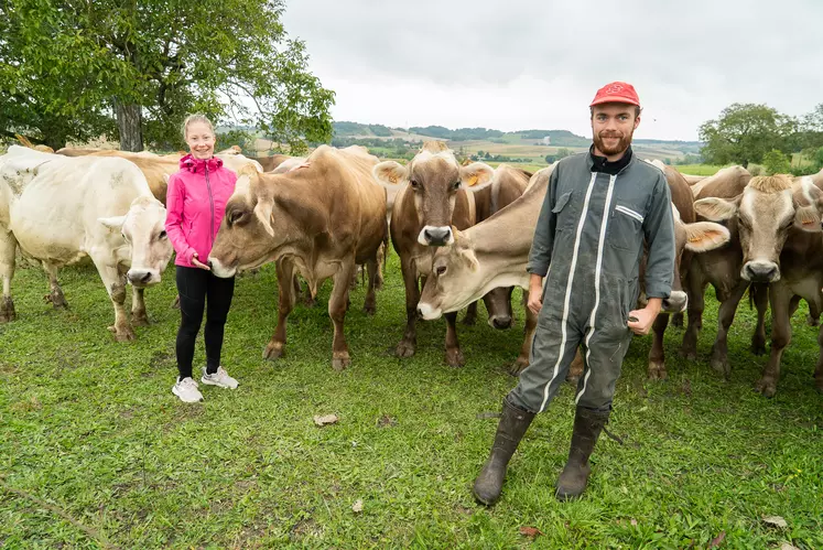 Une jeune femme et un jeune homme souriant devant un troupeau de aches brunes des alpes