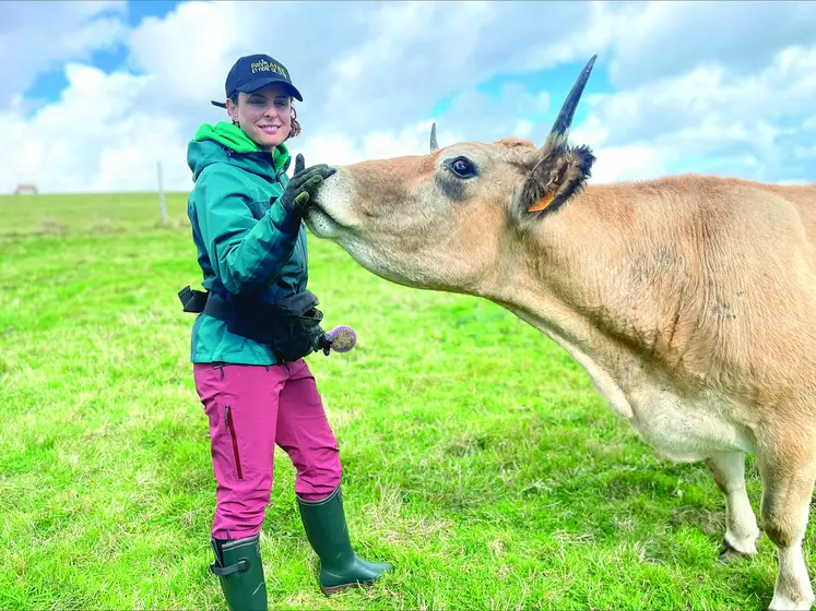 Jeune femme caresse le museau d'une vache dans un pré.
