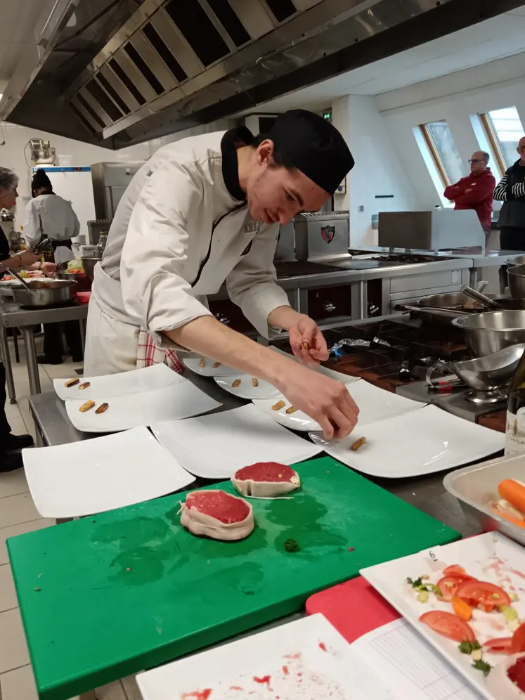 Une jeune cuisinier dresse des pavés de bœuf. 