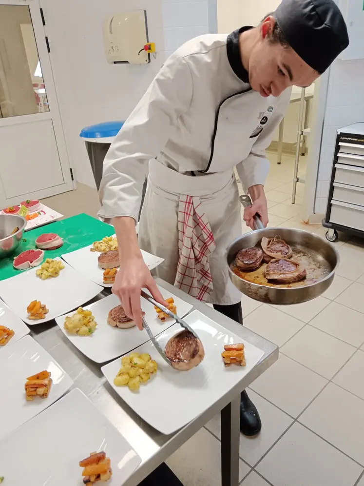 Une jeune cuisinier dresse des pavés de bœuf rôtis dans des assiettes.