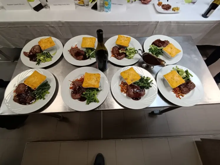 8 assiettes sont dressées avec un pavé de bœuf et des légumes, au milieu une bouteille de vin