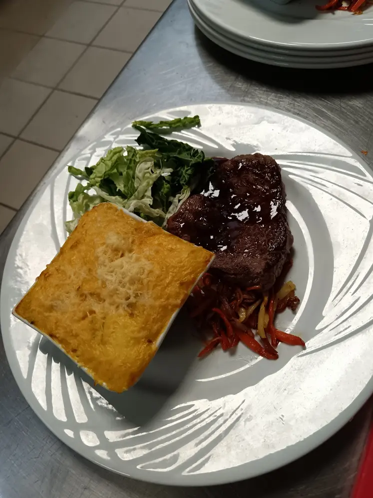 une assiette est dressée avec un pavé de bœuf en sauce, un peu de salade et des légumes