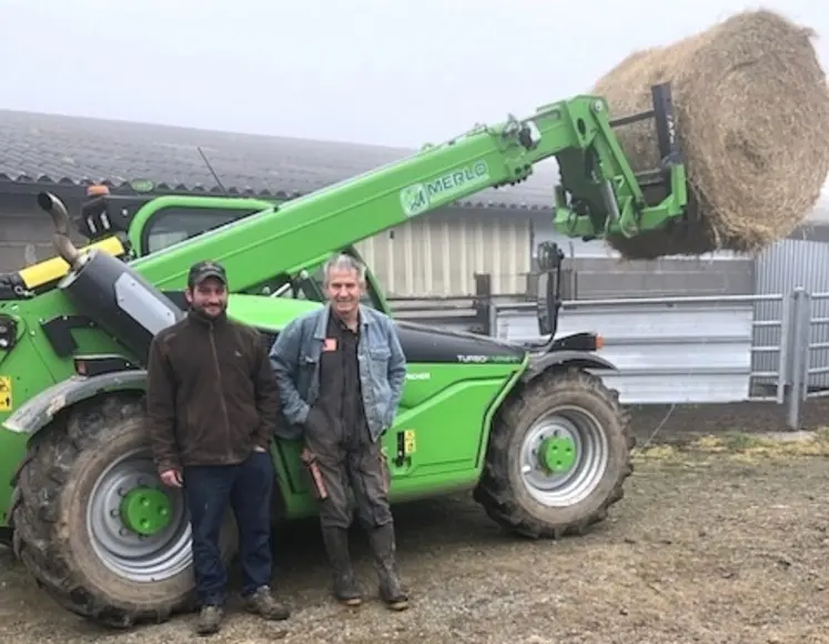 Deux hommes souriants, un jeune et un plus âgé, sont appuyés sur une machine agricole.
