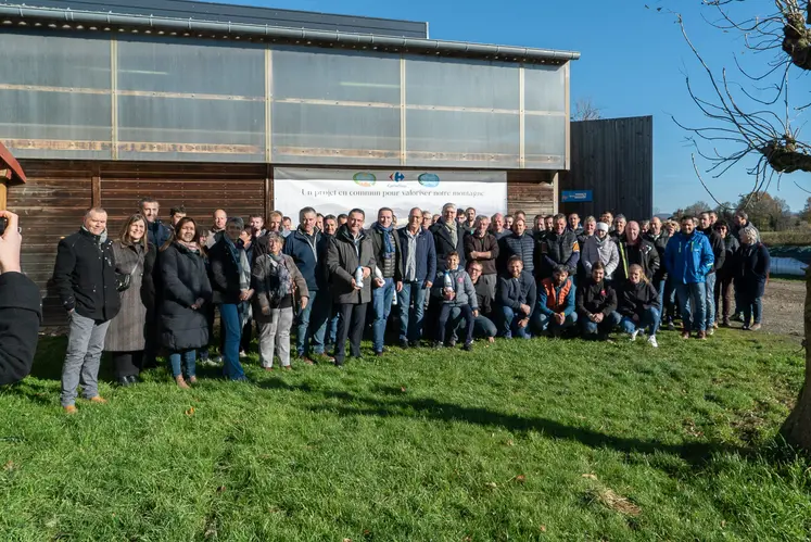 Un grand groupe de producteurs laitiers posent devant une pancarte avec les logos de carrefour, coopal, et slva.