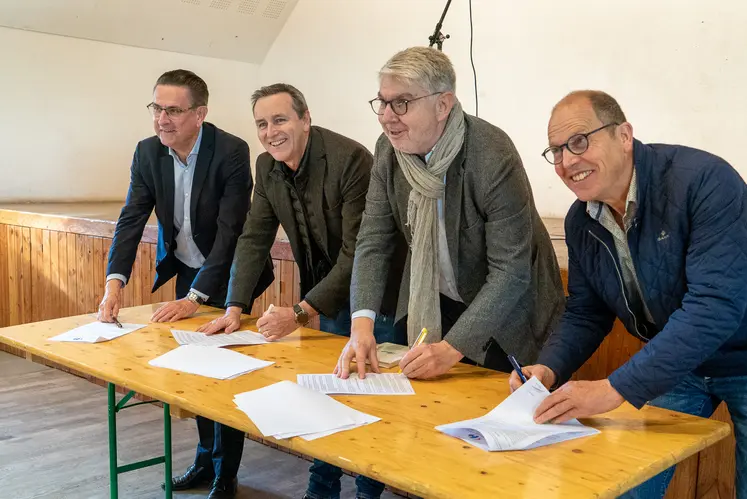 Quatre hommes souriants signent un contrat sur une table.