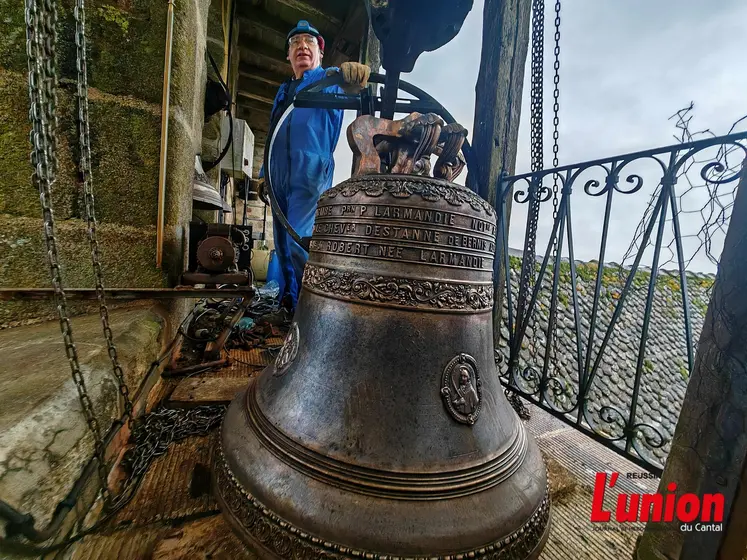 Dans un clocher, un campanaire pose fièrement devant une cloche fraîchement restaurée. 