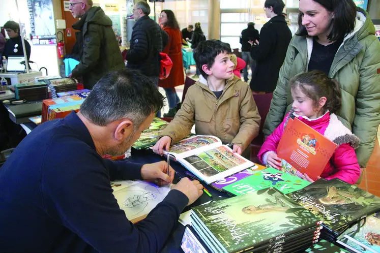 Un dessinateur en train de dédicacer une bande-dessinée à deux enfants et leur maman