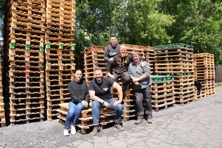 Cinq personnes posant devant des piles de palettes en bois.