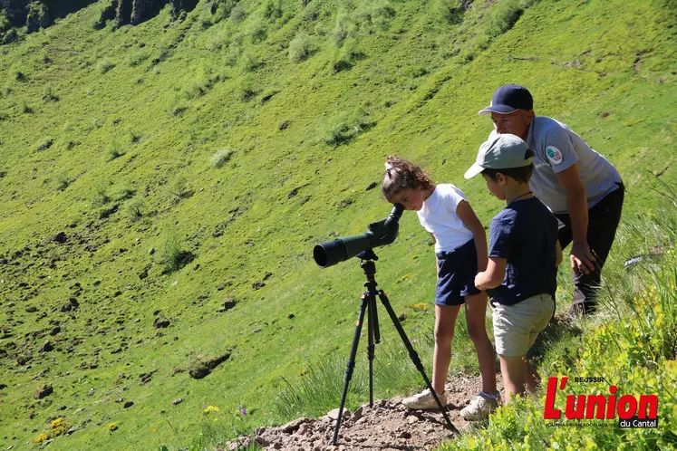 Un homme debout avec des enfants qui regardent un paysage de montagne à la longue vue.
