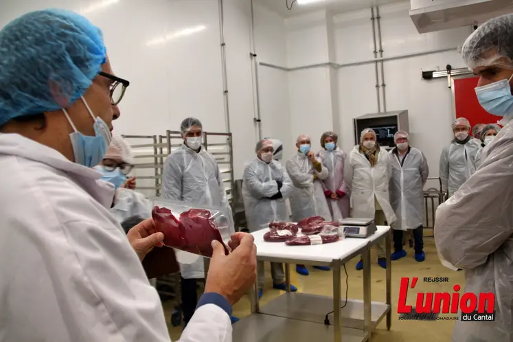 dans un atelier de découpe de viande, un responsable montre à des visiteurs un produit découpé, conditionné sous-vide