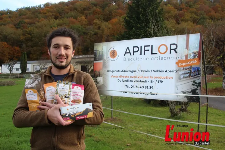 Douglas Estager les bras chargés de biscuits, devant la panneau de la biscuiterie Apiflor