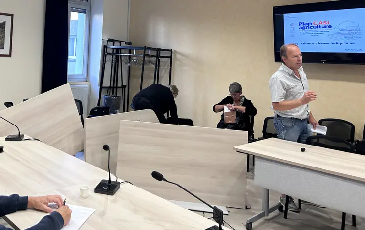 Tables renversées dans une salle de réunion, avec Christian Arvis s'adressant à une personne hors cadre avec une véhémence gestuelle visible.