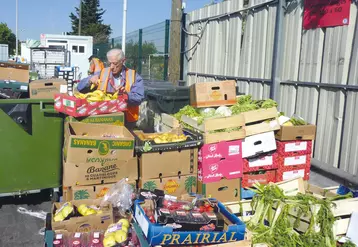 Deux hommes trient des piles de cartons remplis de fruits et légumes.