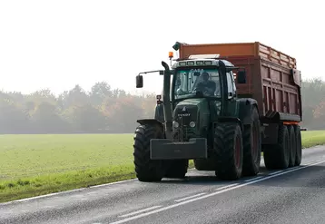 Un tracteur avec remorque roulant sur la route dans la campagne.