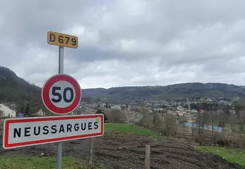 un panneau avec écrit 50 et Neussargues, en arrière plan le village
