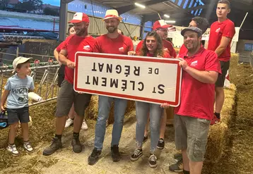 Un groupe de gens tient un panneau signalétique de commune à l'envers dans une étable paillée