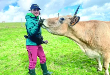 Jeune femme caresse le museau d'une vache dans un pré.