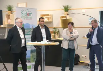 Quatre personne debout devant un kakémono sidam-copamac, l'un d'entre eux parle dans un micro