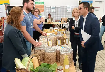 Dans une salle, au milieu d'autres personnes, deux hommes debout parlent autour d'une table avec des produits agricoles