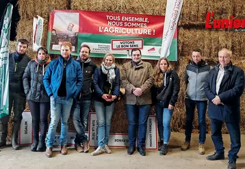 Un groupe d'agriculteurs pose devant des ballots de paille dans un grange de montagne.