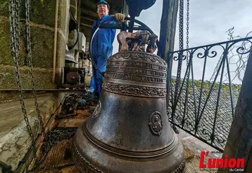 Dans un clocher, un campanaire pose fièrement devant une cloche fraîchement restaurée. 