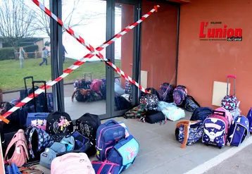 Une entrée d'école fermée par de la rubalise et des cartables restés devant, sans enfant.