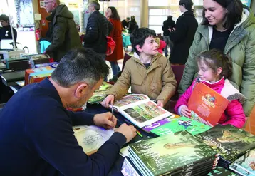 Un dessinateur en train de dédicacer une bande-dessinée à deux enfants et leur maman