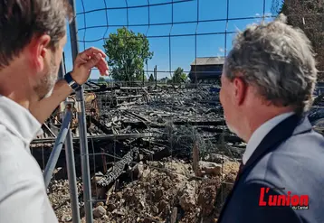 deux hommes de dos observent derrière des grilles un bâtiment calciné.