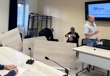 Tables renversées dans une salle de réunion, avec Christian Arvis s'adressant à une personne hors cadre avec une véhémence gestuelle visible.
