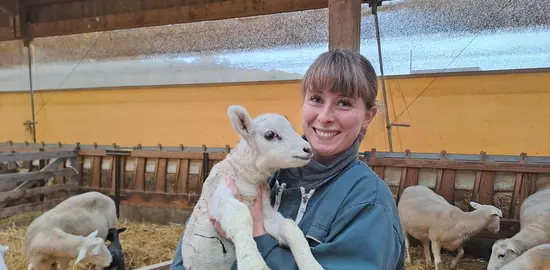 Une éleveuse tient dans ses bras un agneau.