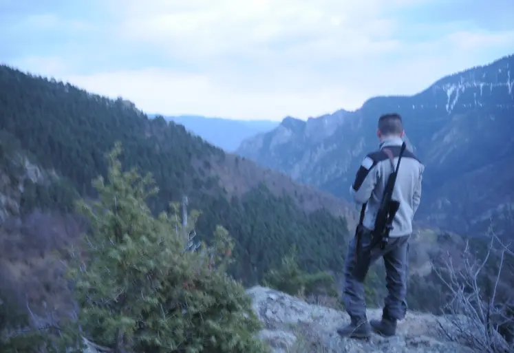 Un chasseur observe une vallée un fusil sur l'épaule.