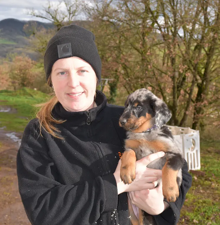 L'éleveuse tient un chiot beauceron dans ses bras en extérieur.