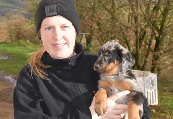 L'éleveuse tient un chiot beauceron dans ses bras en extérieur.