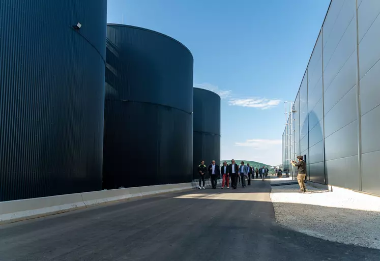 Photo d'une partie des grandes centrales de méthanisation, avec les différentes représentants des organisations du projet marchant à côté. Les centrales sont de grand taille, donnant l'impression que les représentants sont petits. 