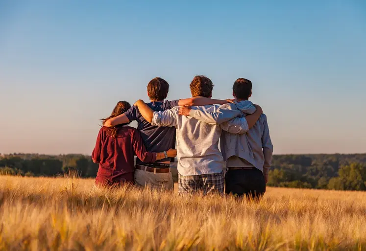 Quatre jeunes de dos se tenant par les épaules au milieu d'un champ.