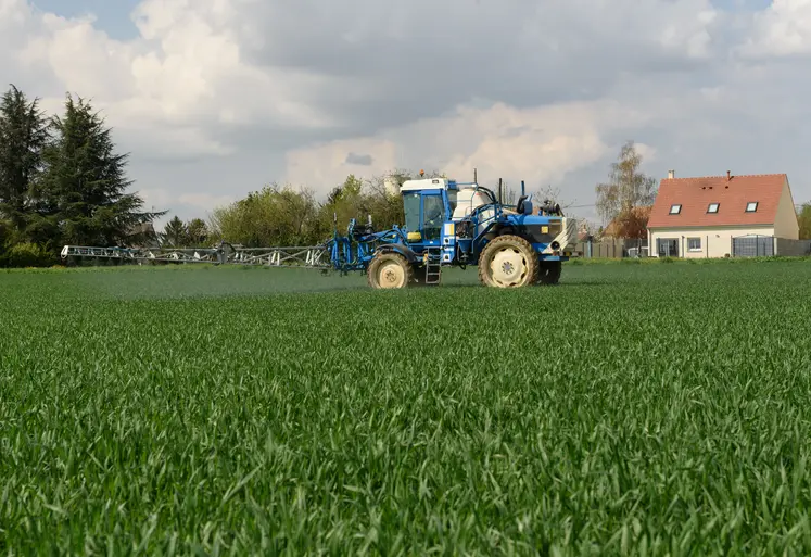 au premier plan un tracteur utilisant des pesticides et en arrière plan une maison