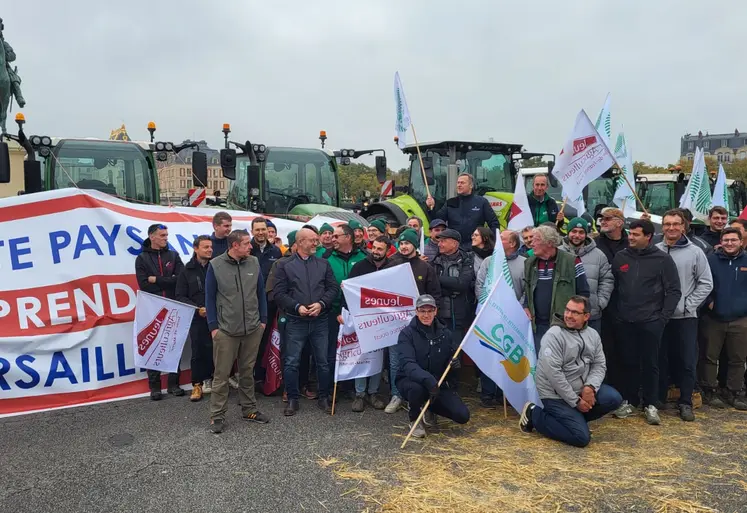 Des agriculteurs sur une botte de paille avec banderole "la révolte paysanne reprend à Versailles" devant le château de Versailles.