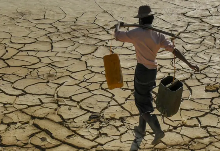 homme transportant sur ses épaules des récipients d'eau et qui marche sur un sol craquelé