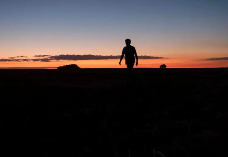 Silhouette d'une personne debout dans un champ avec un coucher de soleil. 